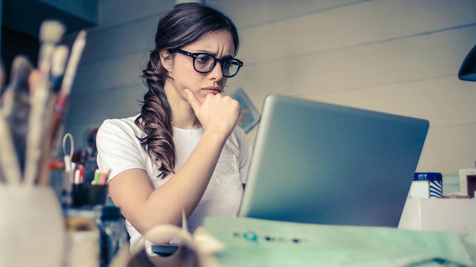 Woman with braided hair and glasses looking concerned at a laptop screen