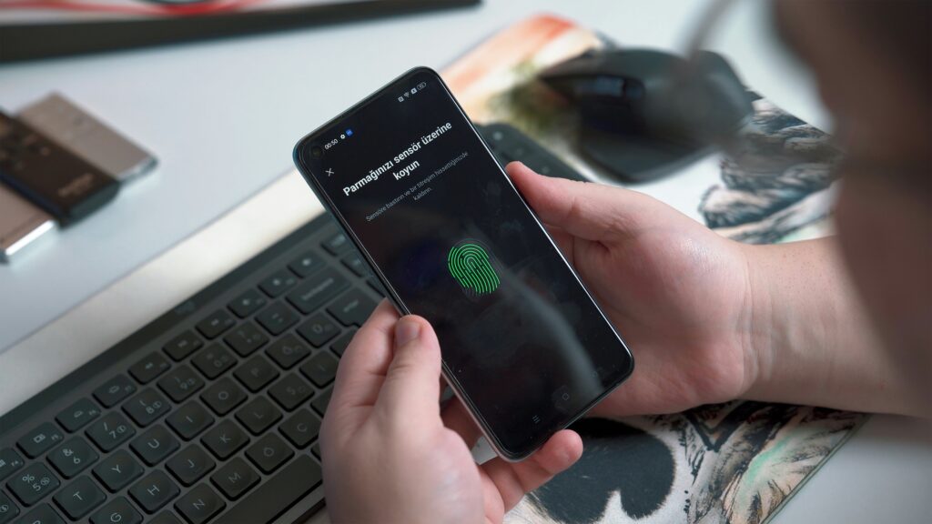 A hand holding a phone unlocking it with a fingerprint scan next to a laptop