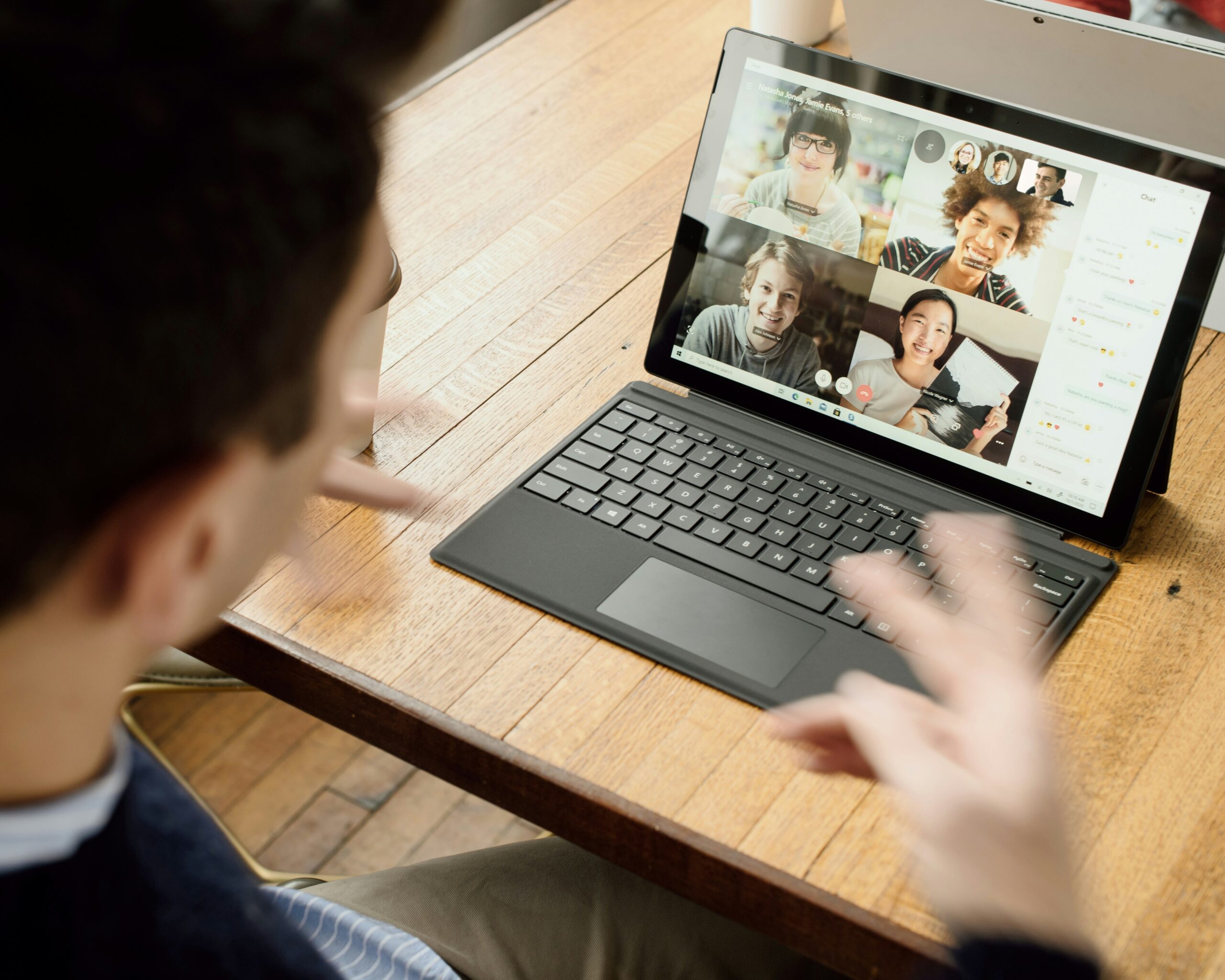 A person on a video call with several other people visible on a laptop screen