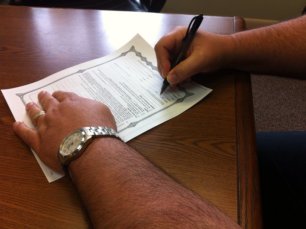 Close-up of hands signing a document on a wooden desk