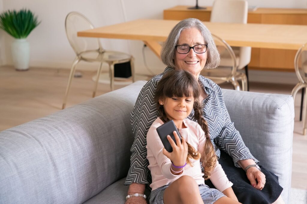 A grandmother and her granddaughter using a phone together at home
