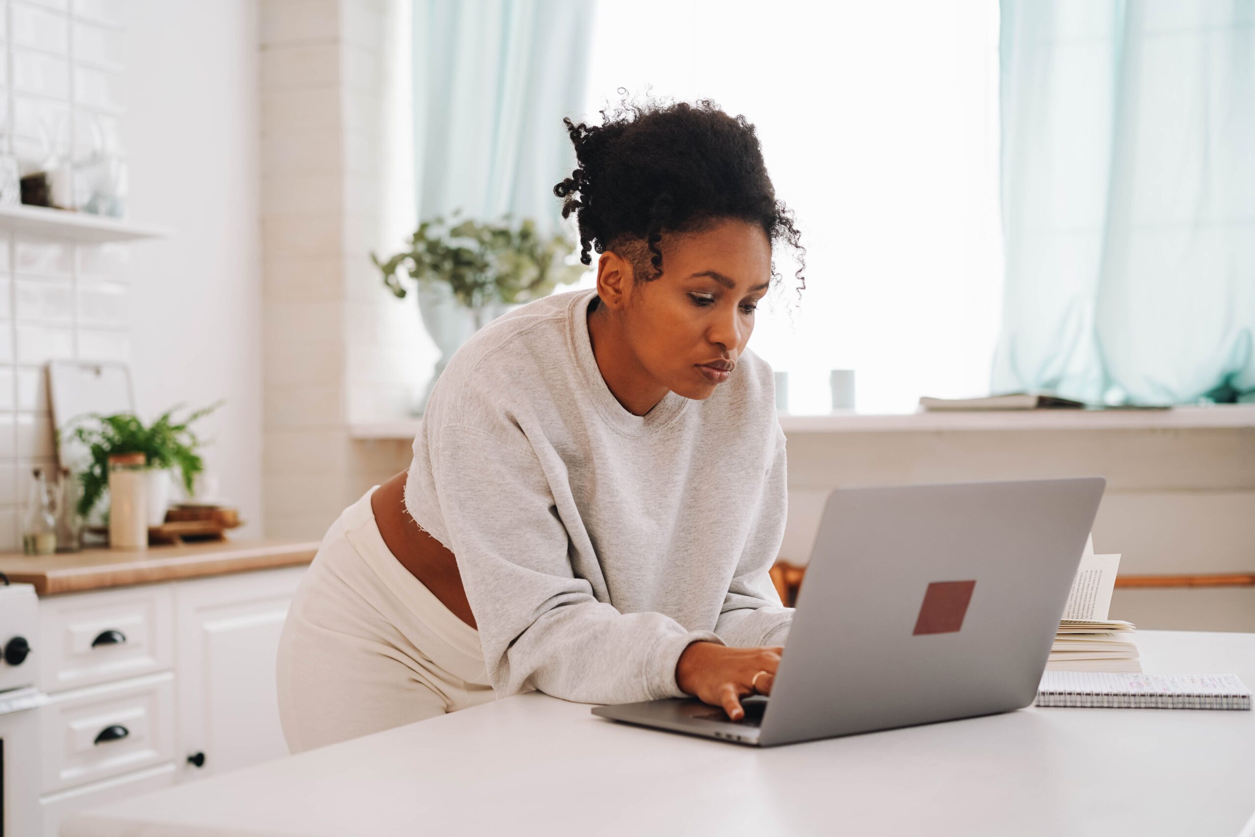 A woman leaning over a laptop with a focused, concerned expression in a bright kitchen