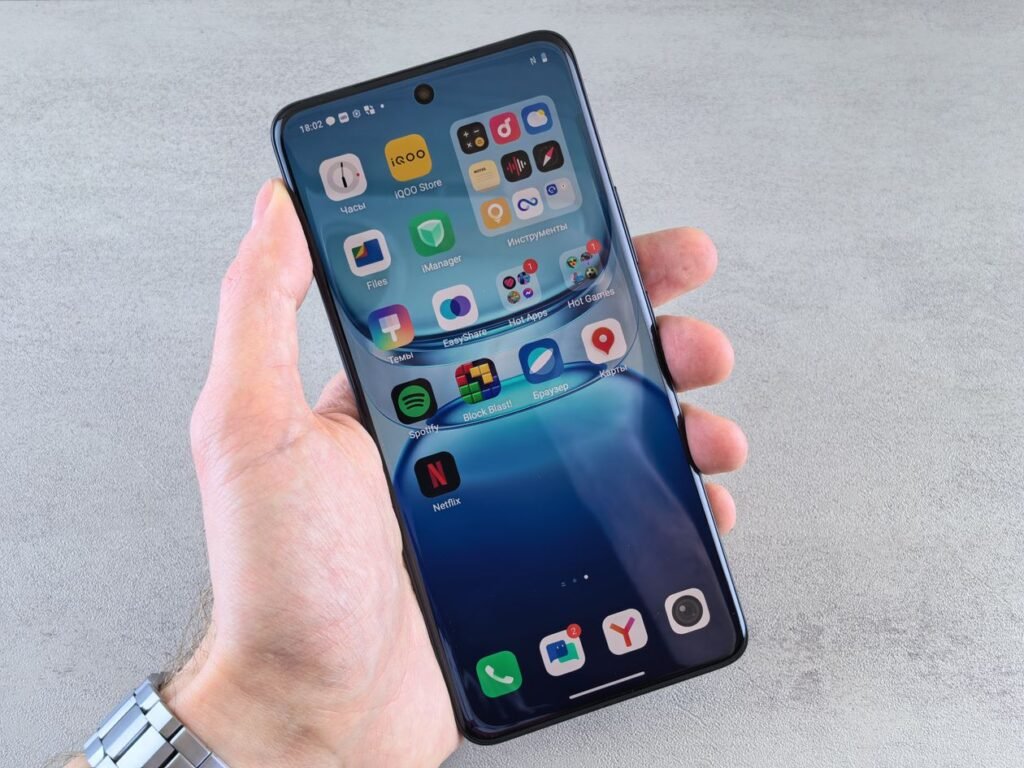 A hand holding a smartphone showing app icons on the home screen