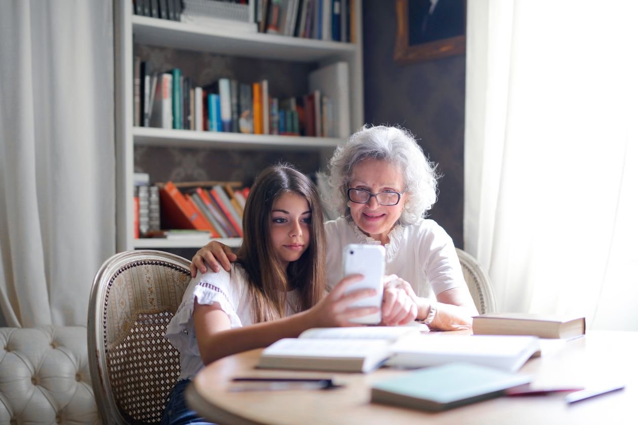 A grandmother and her teenage granddaughter looking at a smartphone together at a table