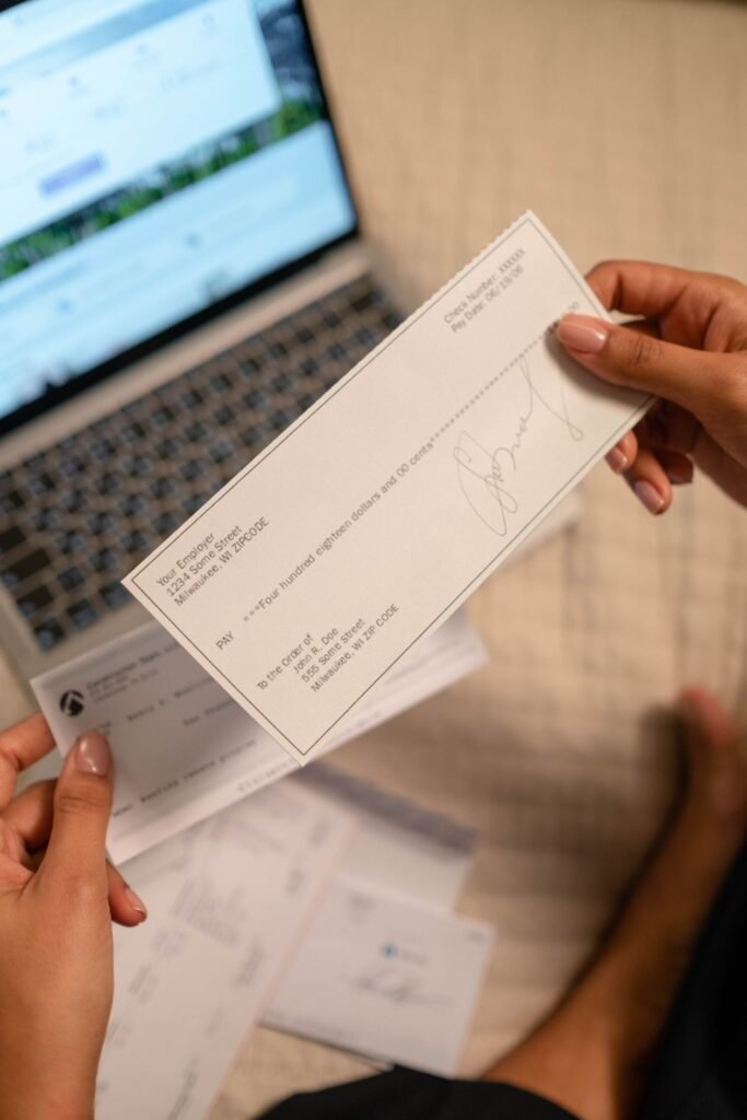 Hands holding a paycheck next to an open laptop